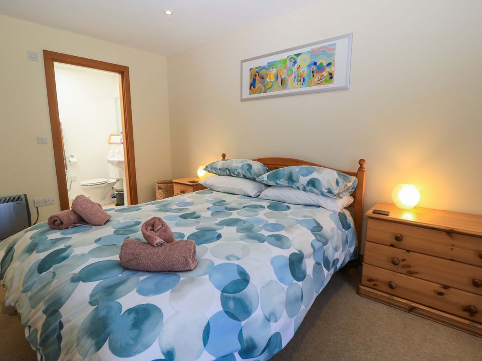 A bedroom with a bed with patterned bedding and two wooden dressers by the bed with lamps at The Old Cart Shed in Winterborne Stickland