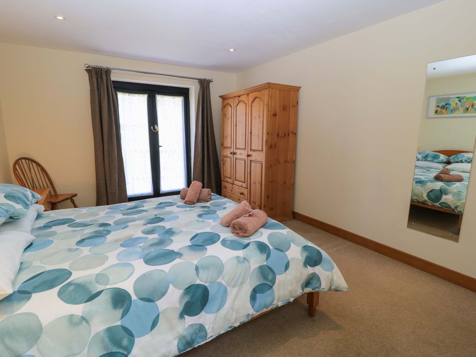 A bedroom with a bed covered in a blue patterned duvet two brown towels on the bed a wooden wardrobe a wooden chair brown curtains and a full-length mirror on the wall at The Old Cart Shed in Winterborne Stickland
