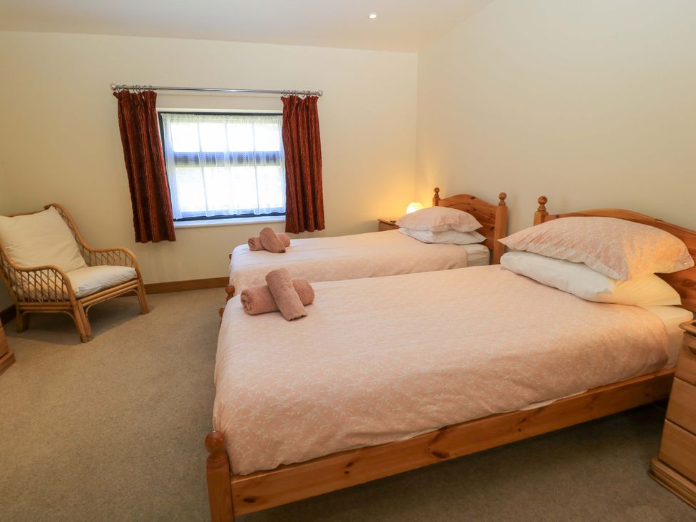 A bedroom with two single beds with pink bedding a wooden chair and a window with red curtains at The Old Cart Shed in Winterborne Stickland