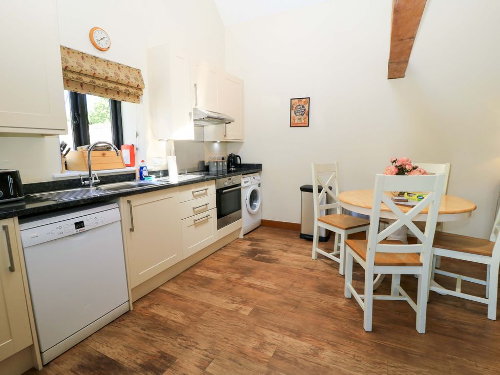 A kitchen with white cabinets a wooden dining table with chairs and a flower vase at Rowdens Barn in Winterborne Stickland