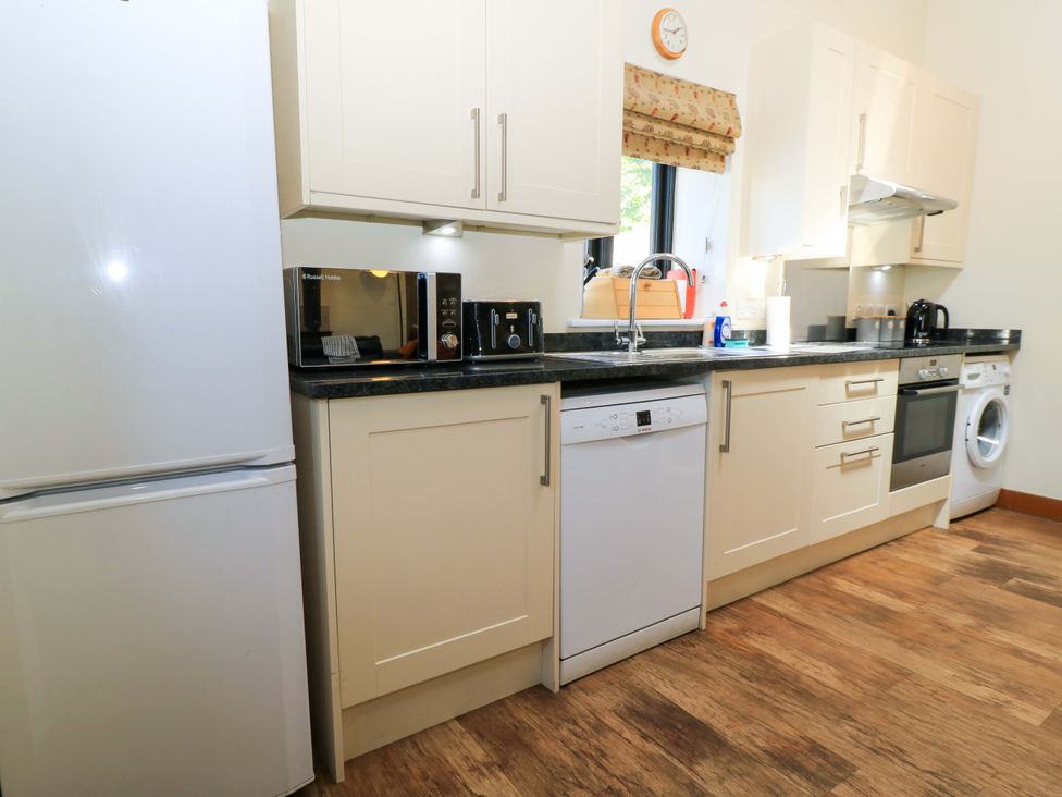 A kitchen with white cabinets appliances including refrigerator microwave toaster dishwasher oven washing machine and a window at Rowdens Barn in Winterborne Stickland