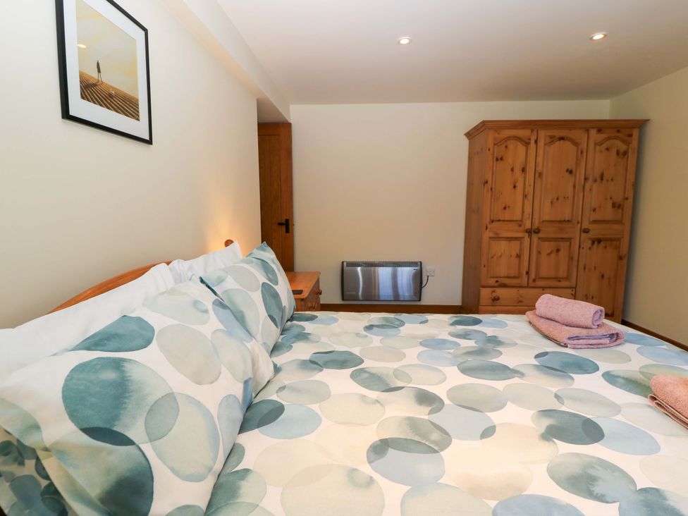 A bedroom with a bed with patterned bedding a wooden wardrobe a wooden door and a wall heater at Rowdens Barn in Winterborne Stickland