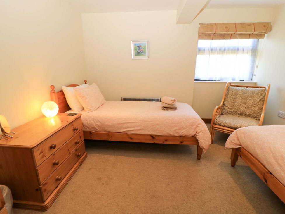 A bedroom with two single wooden beds a wooden chest of drawers a wicker armchair and a window with a valance at Rowdens Barn in Winterborne Stickland