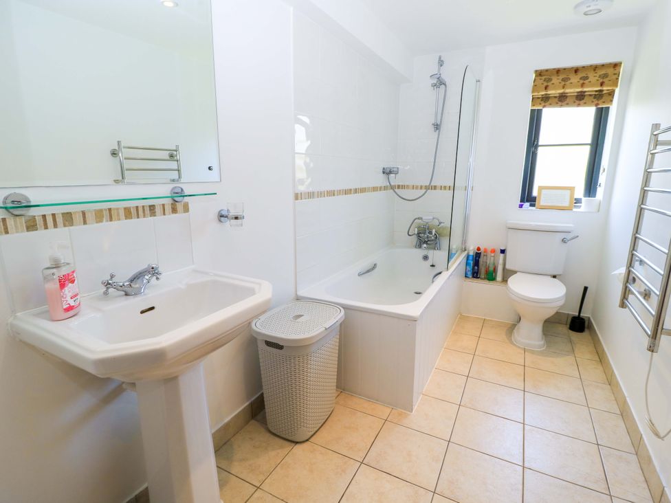 A bathroom with a pedestal sink soap dispenser laundry basket bathtub toilet and window at Rowdens Barn in Winterborne Stickland