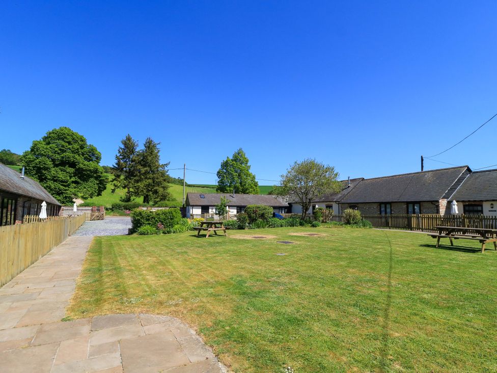 A grassy courtyard with two picnic tables surrounded by buildings and trees at Rowdens Barn in Winterborne Stickland