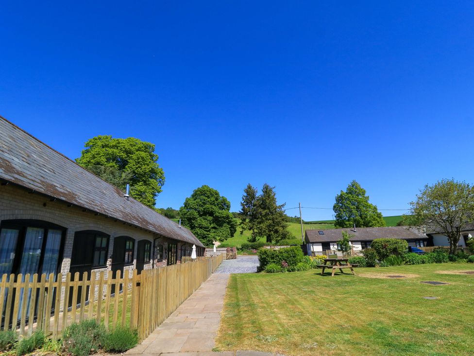 A courtyard with two single-story buildings separated by a lawn and a wooden picnic table at Rowdens Barn in Winterborne Stickland
