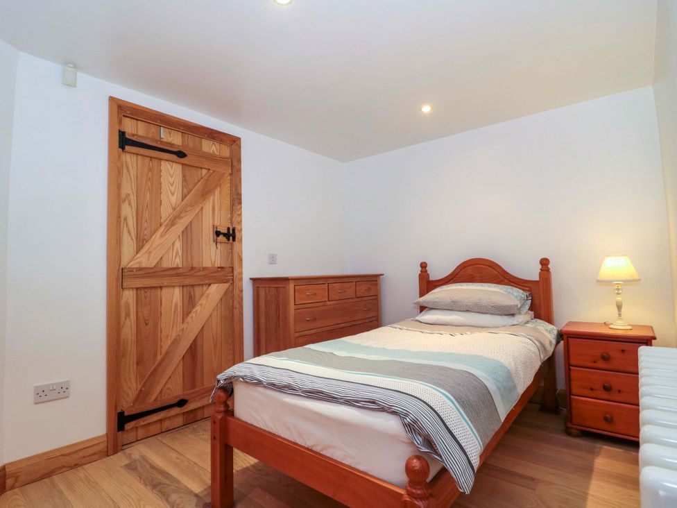 A bedroom with a bed, dresser and lamp at Longside in Gilwern