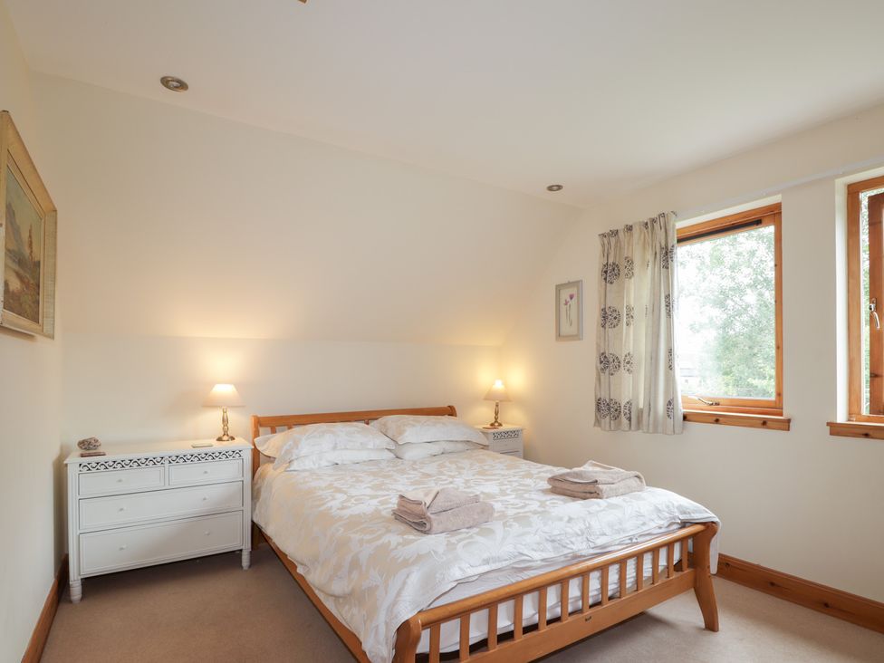 A bedroom with a bed, nightstand, and windows at An Torr in Newtonmore