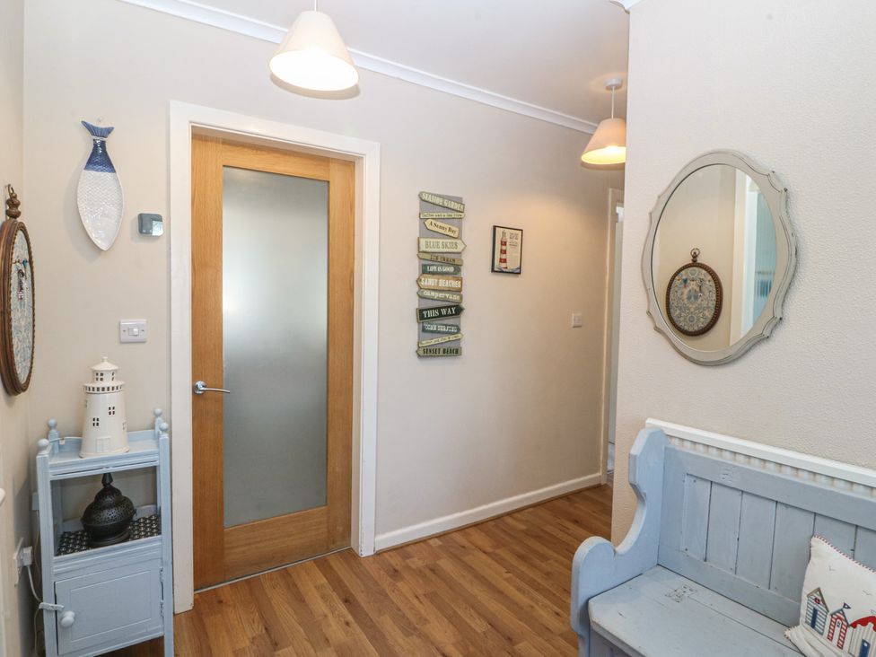 A hallway with a door a bench and wall decorations at Salty Puffin in Benllech