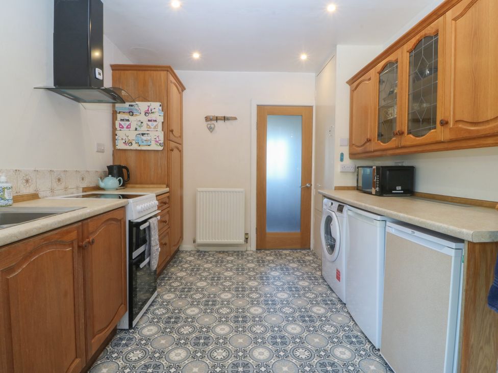 A kitchen with wooden cabinets and appliances at Salty Puffin in Benllech