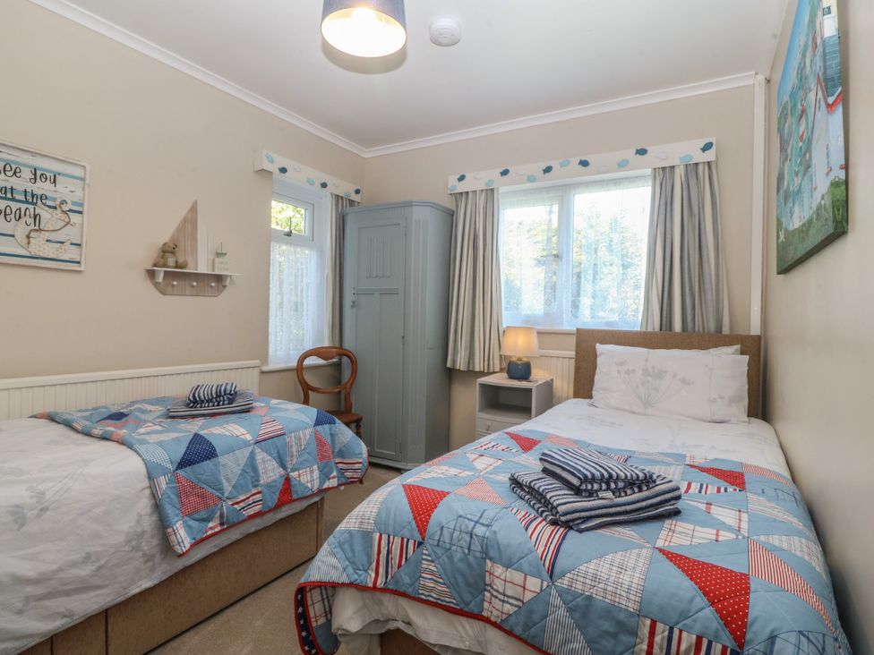 A bedroom with two beds and a wardrobe at Salty Puffin in Benllech