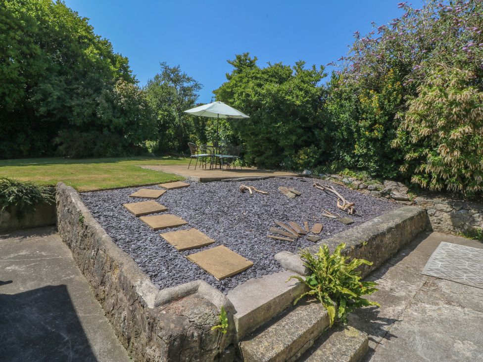 A garden with a stone patio and seating at Salty Puffin in Benllech
