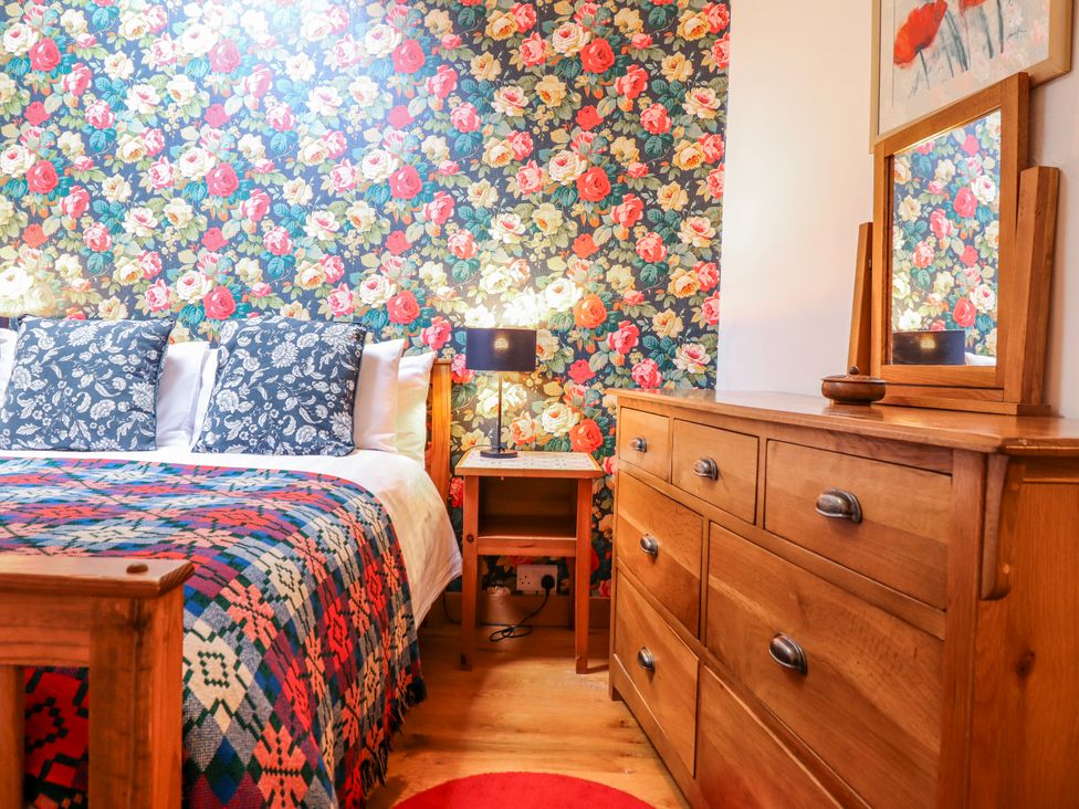 A bedroom with floral wallpaper and wooden furniture at Dovetail Cottage in Llangollen