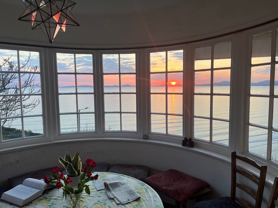 A dining room with a table and flowers overlooking the ocean at Murmur Y Don in Harlech