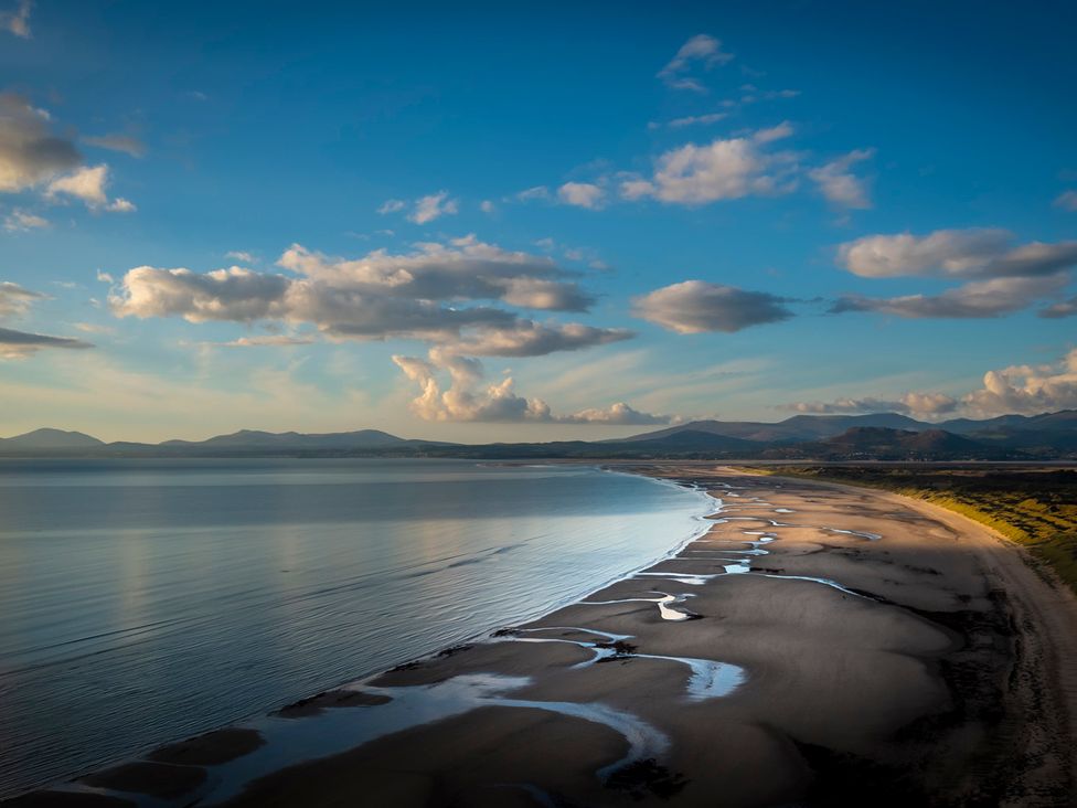 A beach with water and mountains in the background at Murmur Y Don Harlech