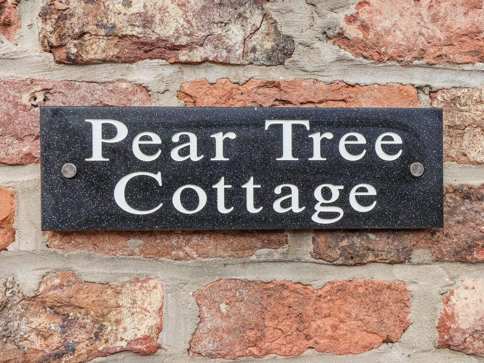 A sign for Pear Tree Cottage on a brick wall in Dunnington