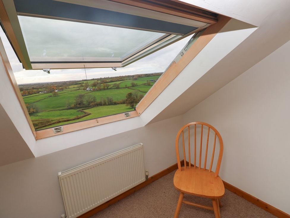 An attic space with a chair and a window overlooking green fields at Bwthyn-y-Rhiw Penybanc near Llandeilo