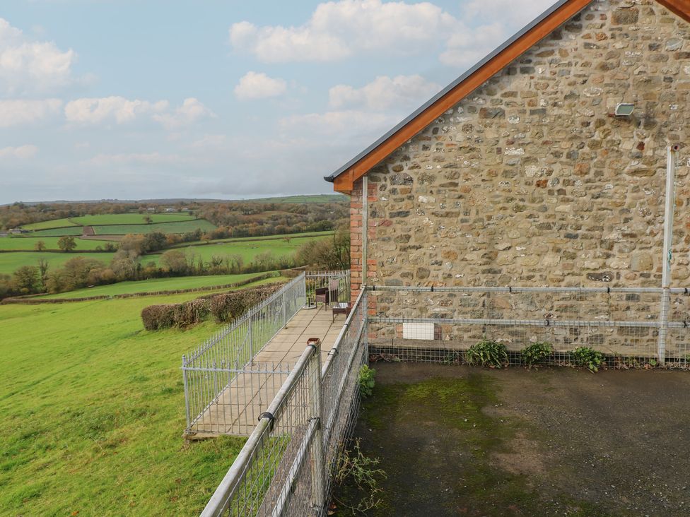 A view of a stone building with a fenced pathway and green fields at Bwthyn-y-Rhiw near Penybanc