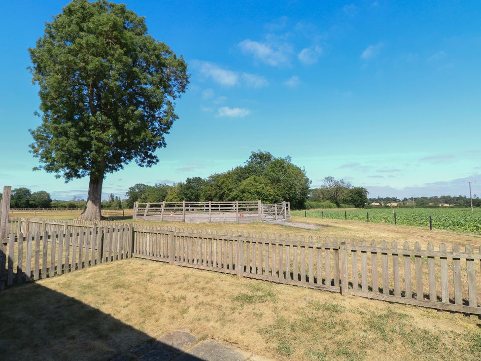 A fenced outdoor area with a tree and a field at Snowy Owl Barn in Shipdham