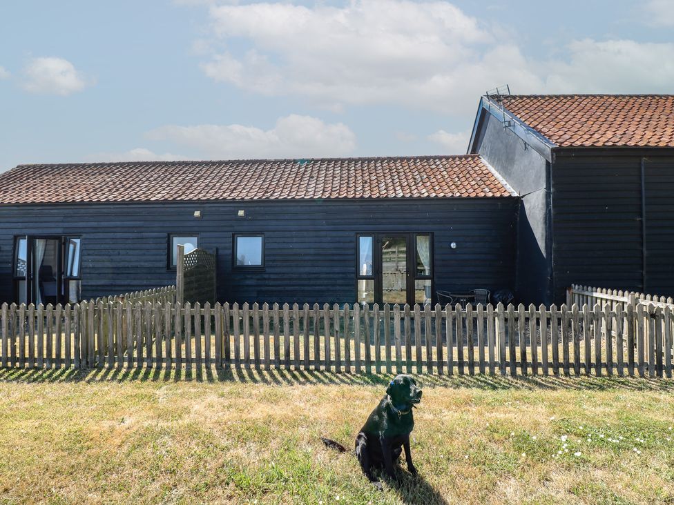 A house with a dog in front and a fence at Tawny Owl Barn Shipdham near Dereham