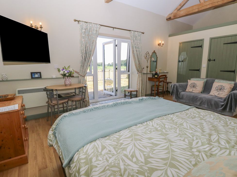 A bedroom with a bed, sofa, table, and doors leading outside at Tawny Owl Barn Shipdham near Dereham