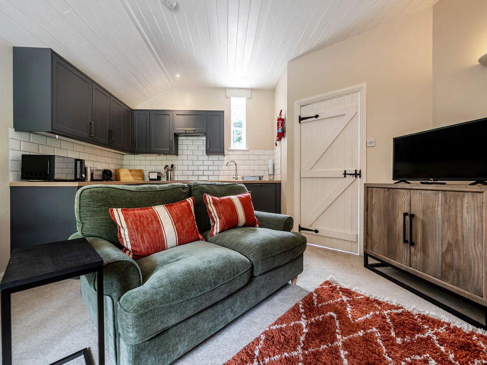 A living room with a sofa and kitchen cabinets at Can Brow at the Graythwaite Estate near Hawkshead
