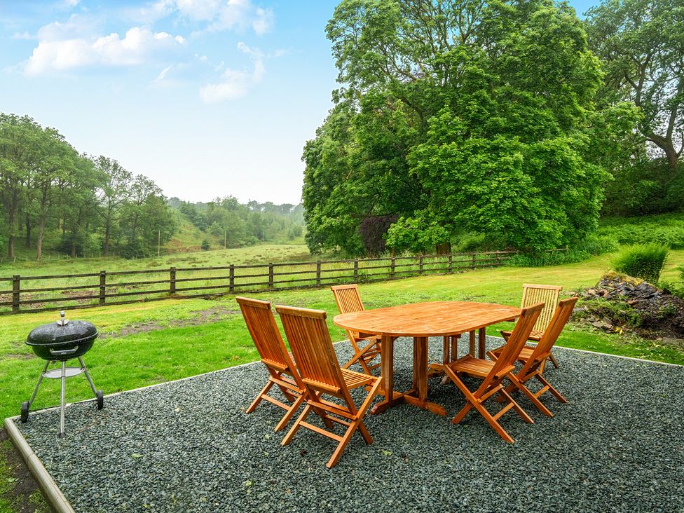 A table and chairs on a gravel patio with a grill in a garden at Jubilee at the Graythwaite Estate near Hawkshead