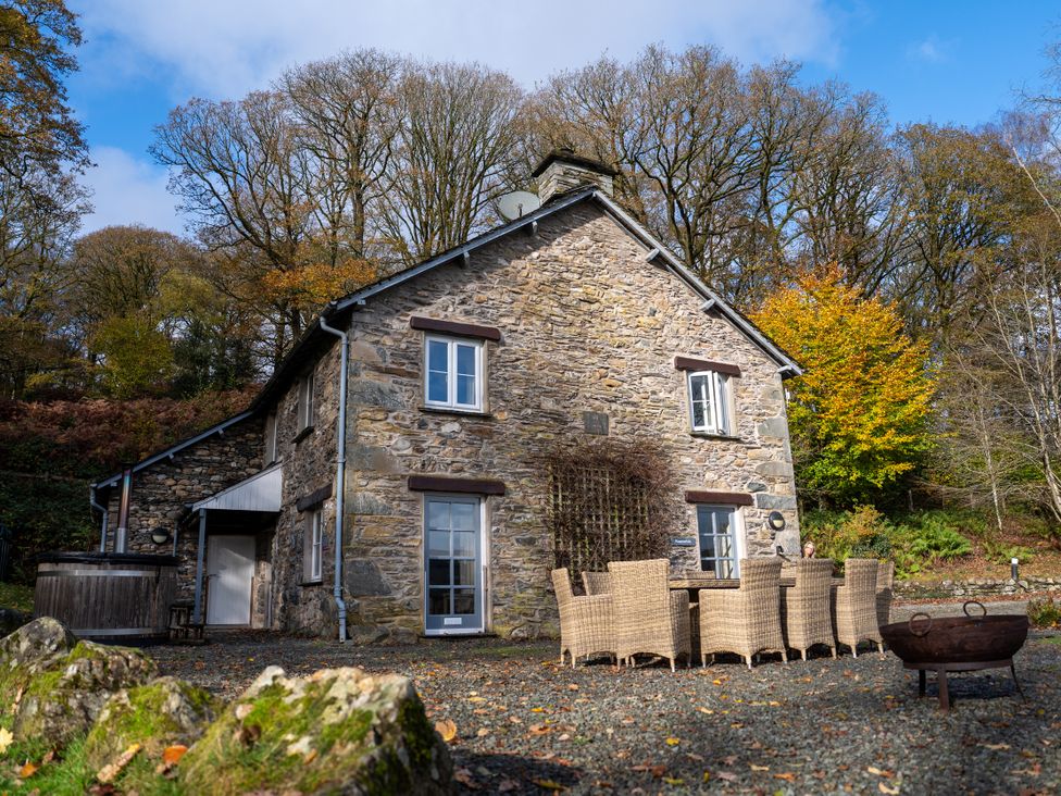 An outdoor view of a stone house with a dining table and chairs at Hammerhole in Graythwaite near Hawkshead