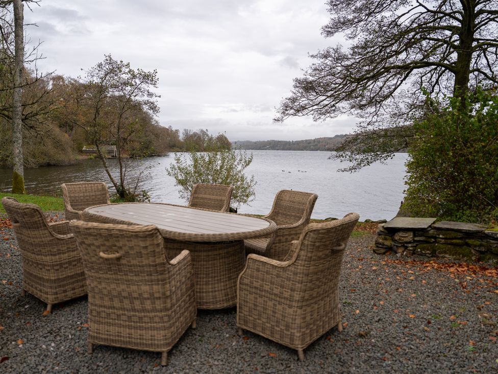 An outdoor seating area with a round table and chairs overlooking a lake at Hullet Hall in Graythwaite near Hawkshead