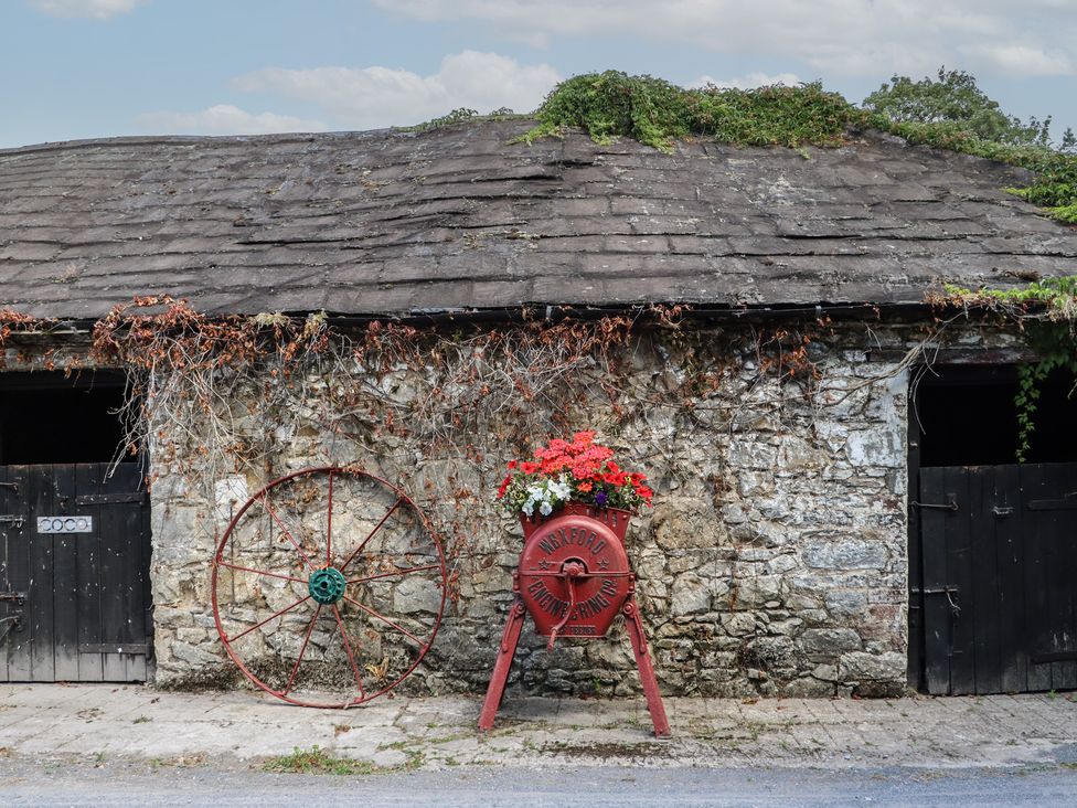 An outdoor view of a stone building with a cart and wagon wheel at Ryan's Loft in Ardfinnan near Clonmel, County Tipperary