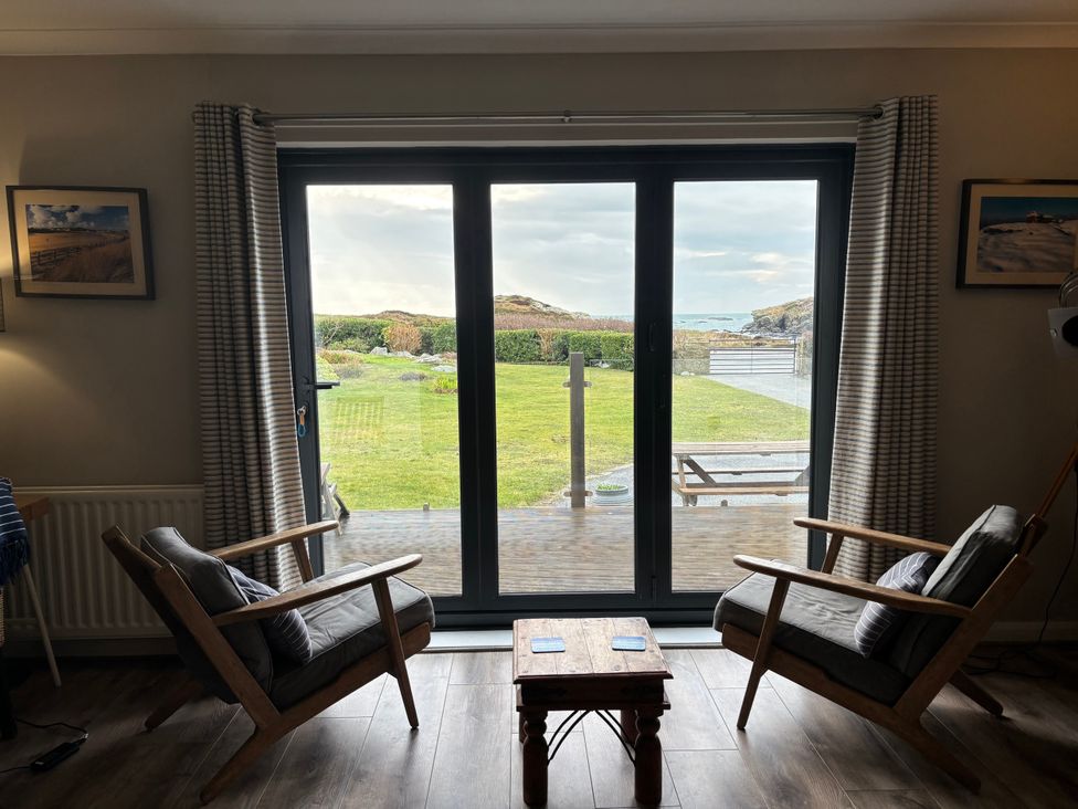 A living room with sliding glass doors and two chairs at The Beach House Trearddur Bay