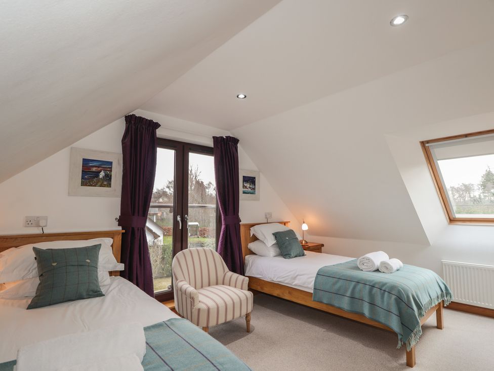 A bedroom with two beds and a chair at Little Chestnut in Muir of Ord