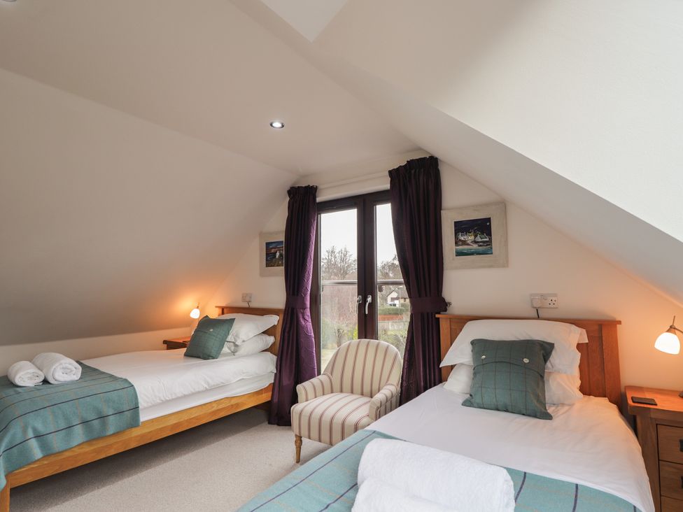 A bedroom with two beds and an armchair at Little Chestnut in Muir of Ord