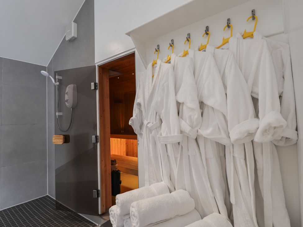 A bathroom with robes on hangers and a sauna door at Little Chestnut in Muir of Ord