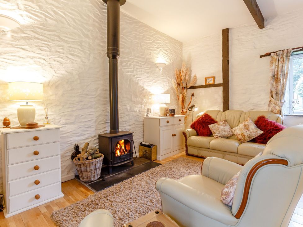 A living room with a wood stove and seating at Wagtail Cottage in East Taphouse