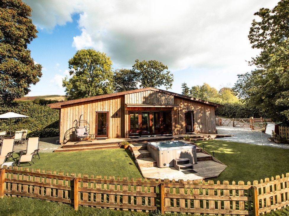 A wooden lodge with a hot tub and garden chairs at Sycamore Lodge Nantmel near Rhayader
