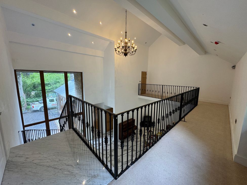 A hallway with a stair railing and chandelier at Plas Glyndwr in Crickhowell