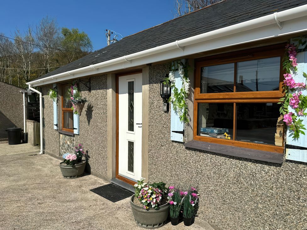 Exterior view of a house with a white door two windows blue shutters and flower pots at The Mill in Abererch near Pwllheli