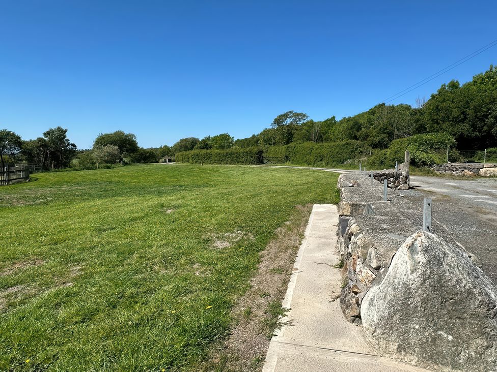 A grassy field with a stone wall and a dirt road under a clear blue sky at The Mill in Abererch near Pwllheli