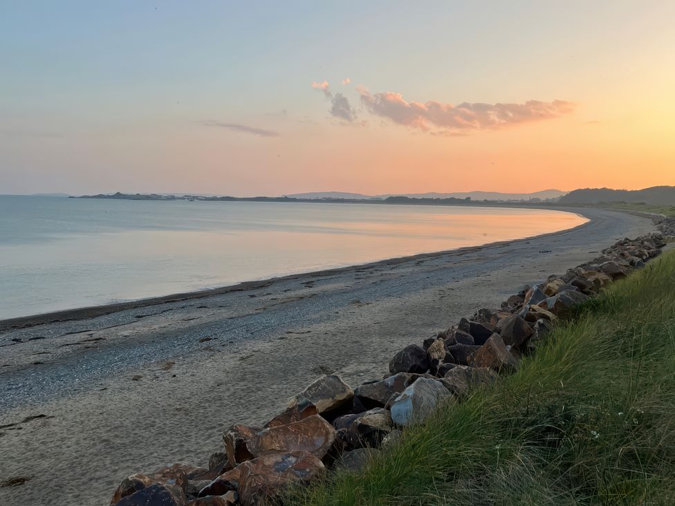 A curved sandy beach with rocks in the foreground and calm sea under a sunset sky at The Mill in Abererch near Pwllheli