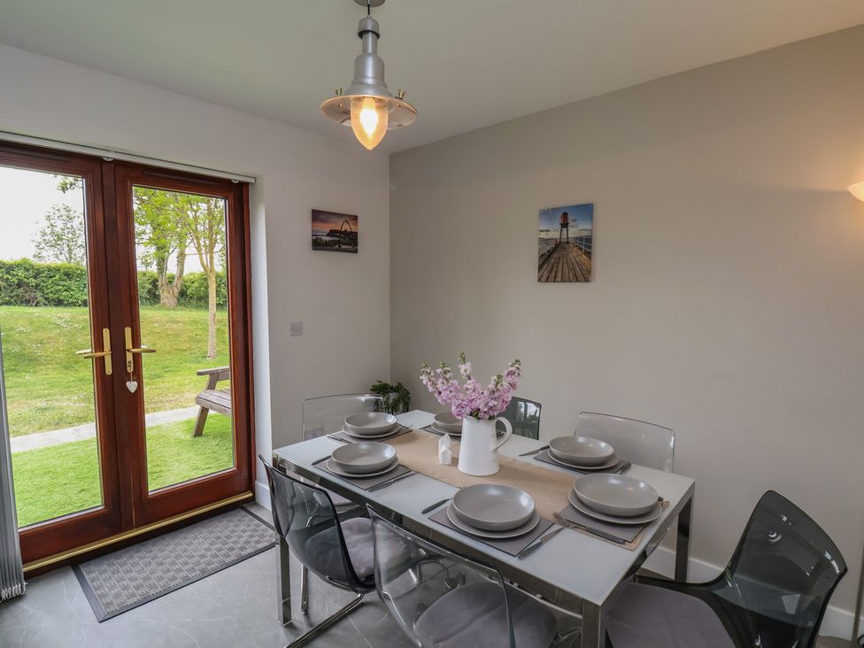 A dining area with a set table of six, transparent chairs, a vase with flowers, and glass doors showing a garden at Buffers in Whitby