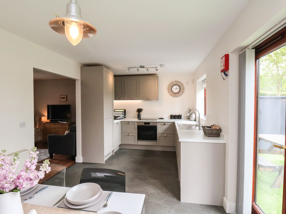 A kitchen with grey cabinets and white countertops next to a dining table with plates and flowers at Buffers in Whitby