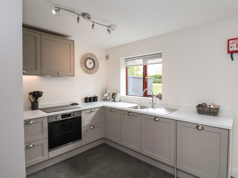 A kitchen with grey cabinets an oven a stove a sink a window and a clock on the wall at Buffers in Whitby