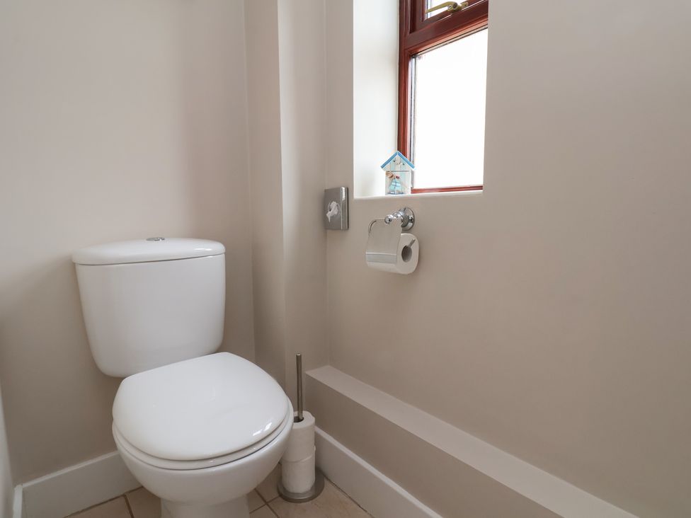 A bathroom with a white toilet a toilet brush holder a window and a toilet paper holder at Buffers in Whitby