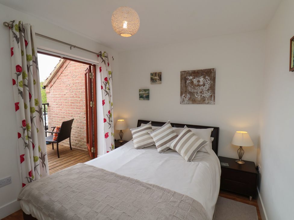 A bedroom with a bed with striped pillows two bedside tables with lamps and a door leading to a balcony at Buffers in Whitby