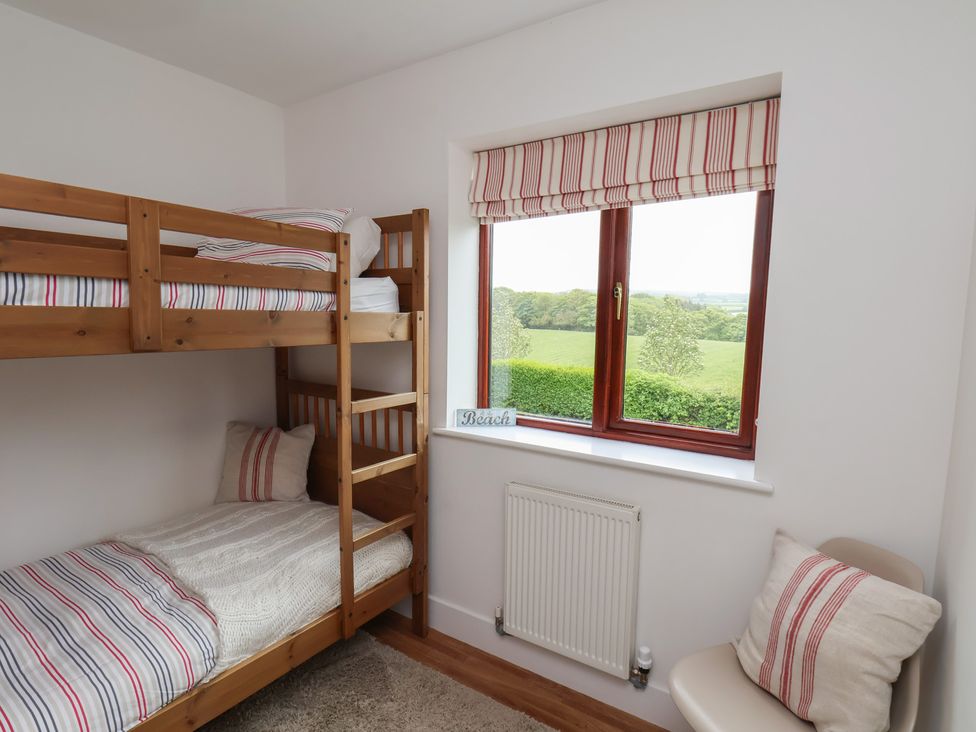 A bedroom with wooden bunk beds next to a window with striped blinds and a chair with a cushion at Buffers in Whitby