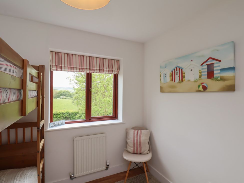 A bedroom with a bunk bed a window with striped blinds a chair with a cushion and a beach scene painting at Buffers in Whitby