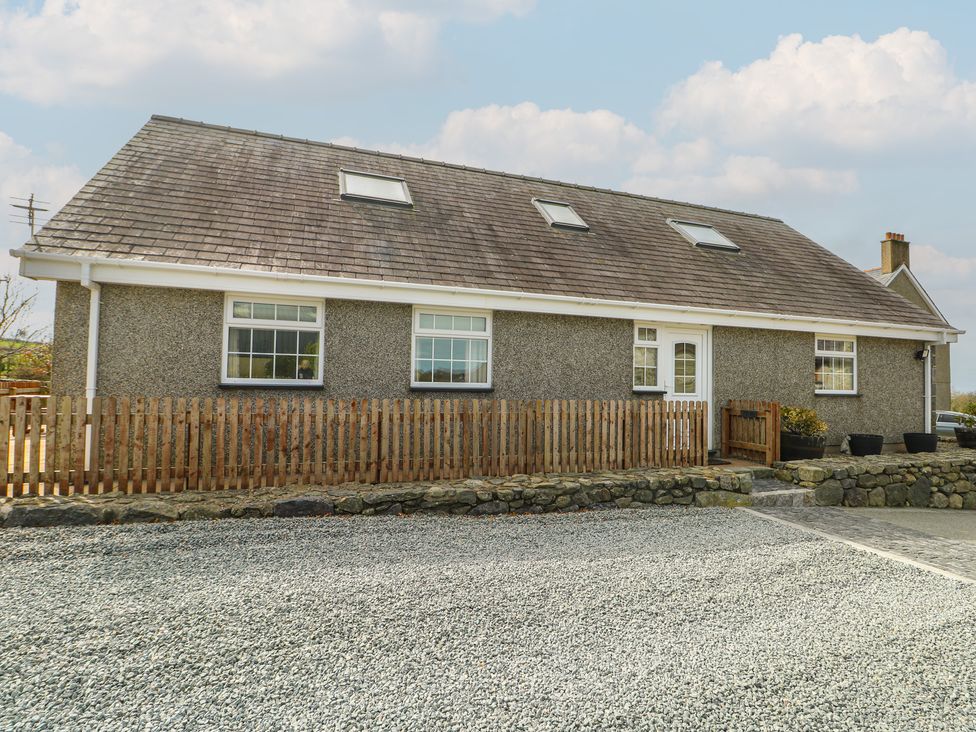 A house with a gravel driveway and a wooden fence at Ty Ni Caeathro near Caernarfon