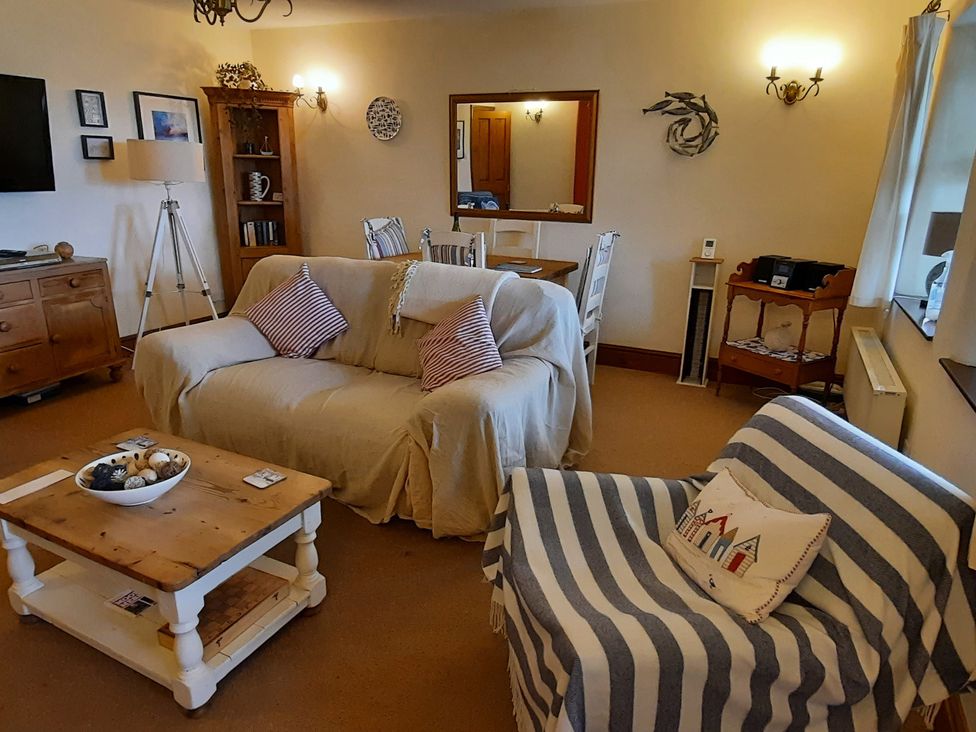 A living room with a sofa, coffee table, and dining table at 4 Cliff Cottages