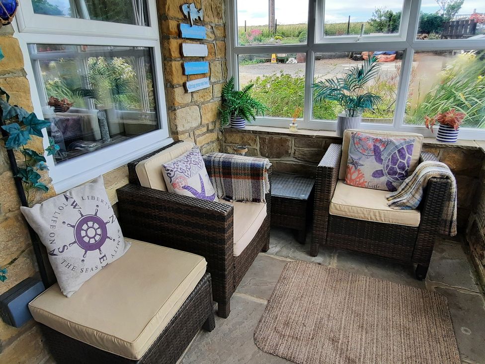 A conservatory with two armchairs and a side table at 4 Cliff Cottages